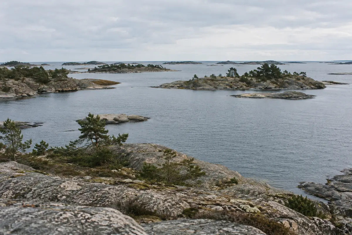 Många små klippöar omgivna av hav, sedda från en stenig strand.